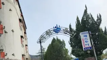 덕원온천 외부 입구 아치형 간판과 주변 나무 전경